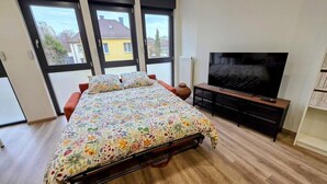 Een slaapkamer met een bed, een televisie en grote ramen.