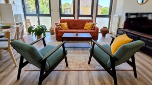 Een moderne woonkamer met een bank, twee fauteuils, een salontafel en een televisie.