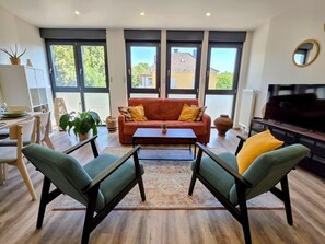 Ein modernes Wohnzimmer mit einer Couch, zwei Sesseln, einem Couchtisch und einem Fernseher.
