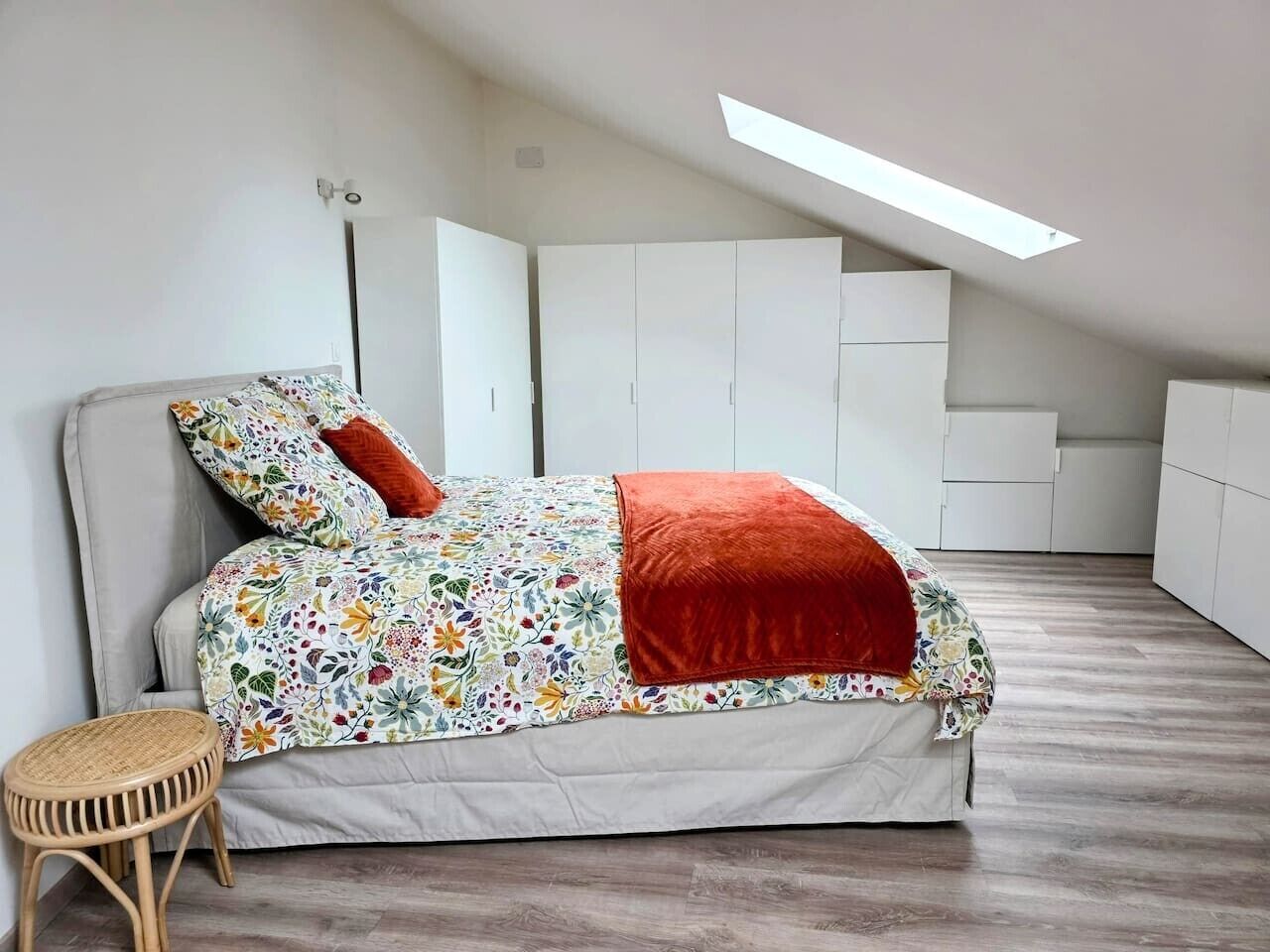 Ein Schlafzimmer mit einem Bett, einem kleinen Hocker und einem Oberlicht.