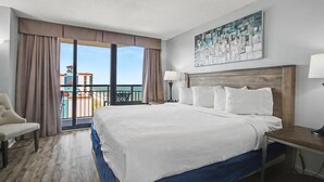 Quarto de hotel com uma cama grande, uma poltrona, uma escrivaninha, um abajur e vista para o oceano.