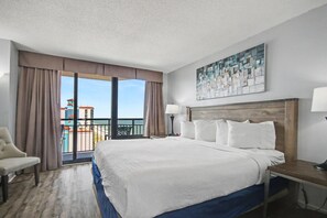 Ein Hotelzimmer mit einem großen Bett, einem Sessel, einem Schreibtisch, einer Lampe und Blick auf den Ozean.