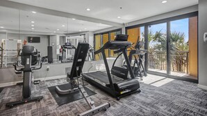Academia com esteiras, bicicletas ergométricas e um espelho grande.