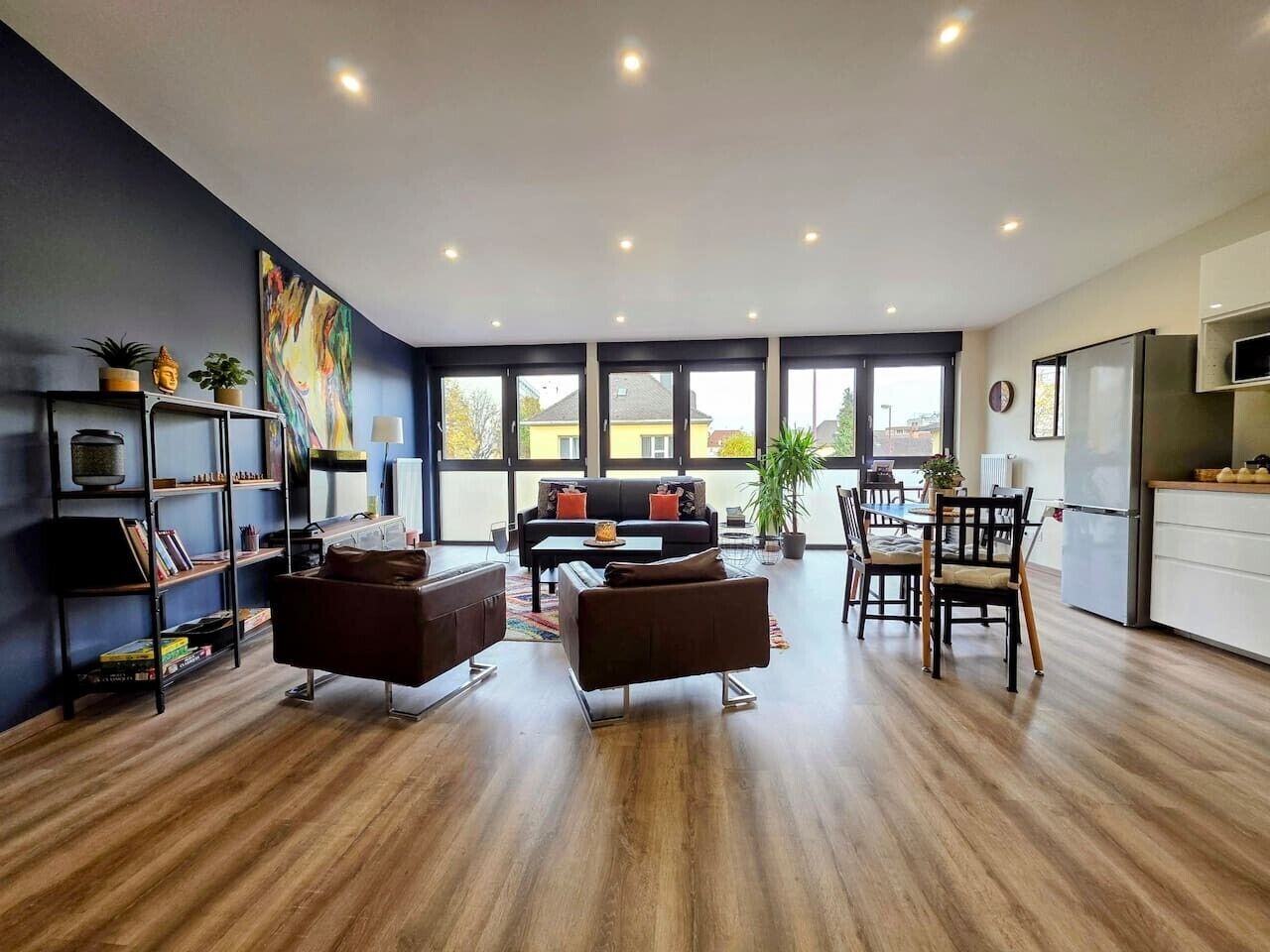 Ein stilvolles Wohnzimmer mit einer Couch, einem Couchtisch und einem Essbereich. Ein Bücherregal und ein großes Fenster sorgen für natürliches Licht.