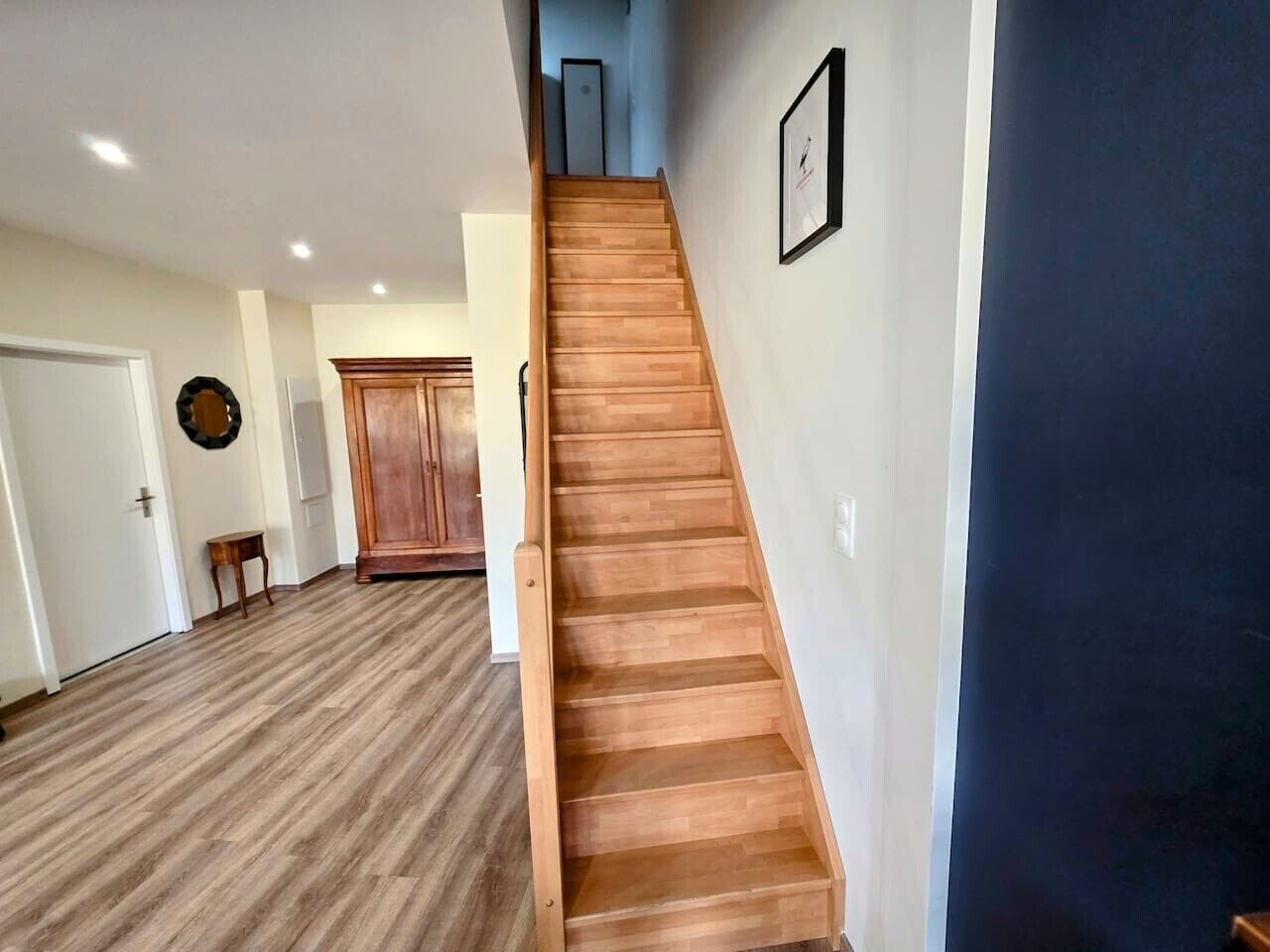 Una escalera de madera con peldaños que conducen a una plataforma, un armario de madera y una pequeña mesa en una habitación con piso de madera.
