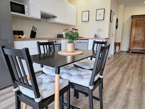A modern kitchen with white cabinets, a microwave, and a dining area with a black table and cushioned chairs. - Charming 55-square-meter duplex, 15 minutes from Strasbourg (Schiltigheim)