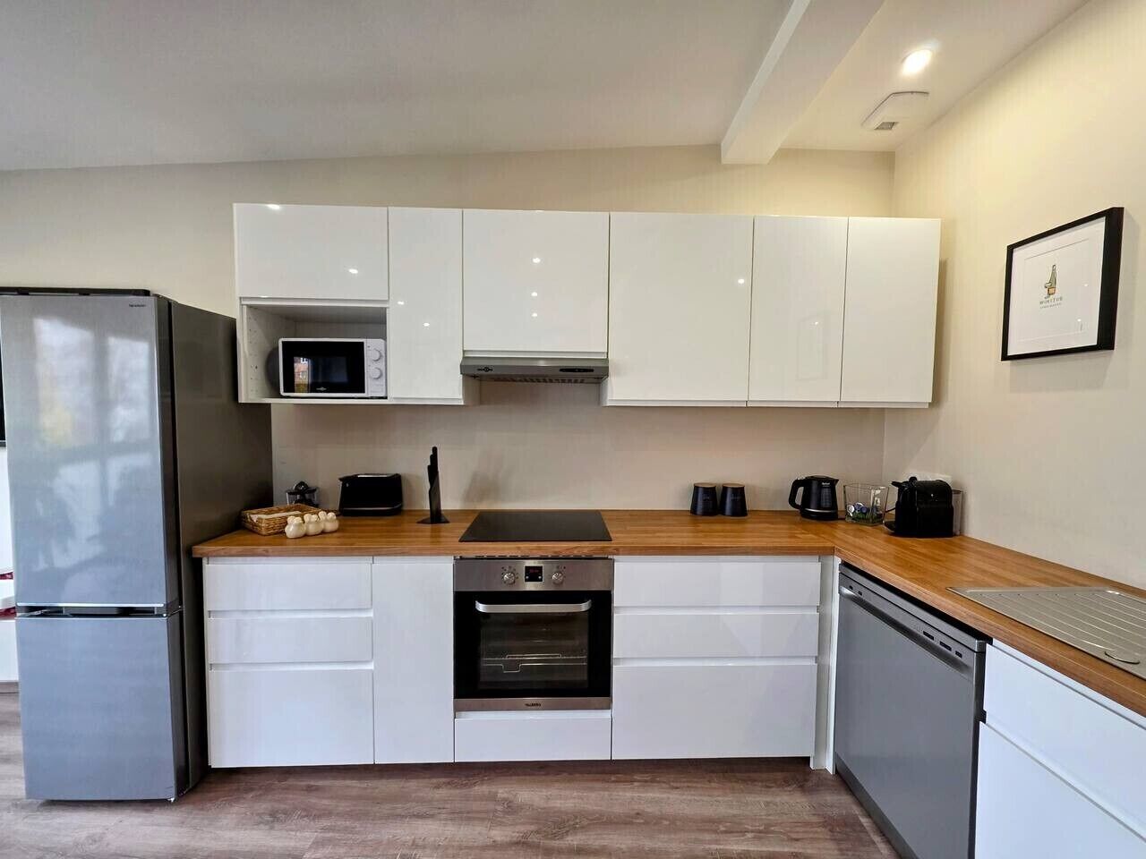 Eine moderne Küche mit weißen Schränken, einem Edelstahl-Kühlschrank, einer Mikrowelle, einem Backofen und einem Geschirrspüler.