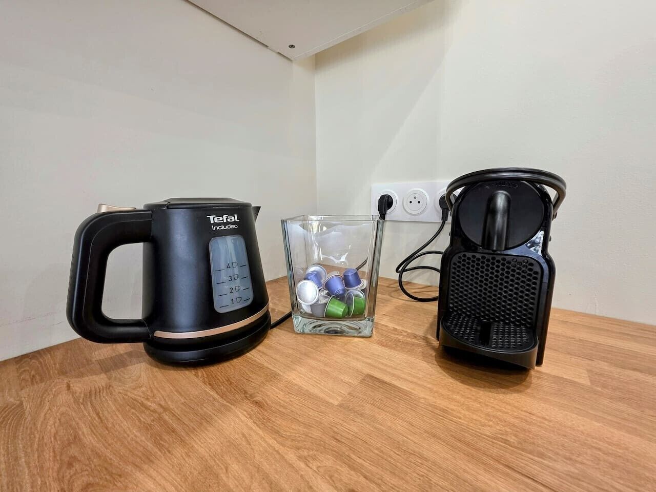 En vattenkokare från Toffel, en behållare i glas med lock av metall och en svart kaffebryggare, placerade på en träyta.