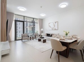 A modern living room with a sofa, coffee table, and dining table set for six. - Vogue, Acacia Direct Access to Dubai Hills Park (Dubai)