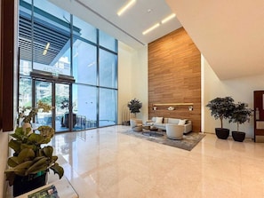 A modern lobby with a glass entrance, a wooden accent wall, and a seating area with a coffee table. - Vogue, Acacia Direct Access to Dubai Hills Park (Dubai)