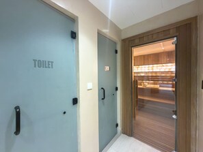A hallway with a toilet door, a mirror, and a wooden door leading to a room with a tiled floor. - Vogue, Acacia Direct Access to Dubai Hills Park (Dubai)