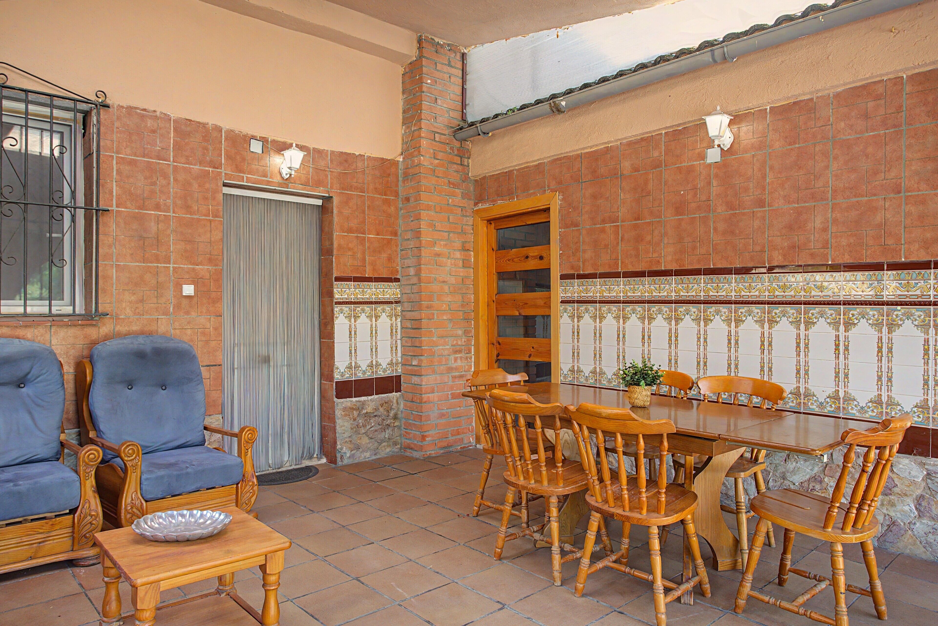Un patio con una mesa y sillas, un sofá azul y una pared decorativa con azulejos estampados.