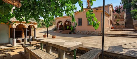 A courtyard with a stone bench, a table, and a building with arches and a tiled roof.