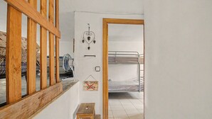 A room with a bunk bed, a wooden stool, a fan, and a 'no shoes' sign.