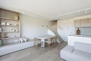 A modern interior with a dining area, built-in seating, a staircase, and a kitchen. - Luxury Duplex "Ondune" - Duinpark Oostduinkerke (Koksijde)