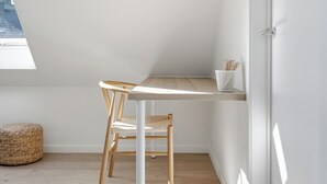 Een compacte, moderne kamer met een schuine kap, een houten bureau, een stoel en een witte deur.