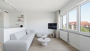 Een moderne woonkamer met een witte bank, een ronde salontafel en een flatscreen televisie aan de muur.