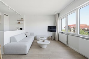 A modern living room with a white sofa, a round coffee table, and a flat-screen TV mounted on the wall. - Luxury Duplex "Ondune" - Duinpark Oostduinkerke (Koksijde)