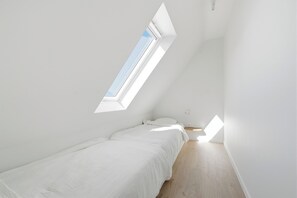 A small, white, single-bed room with a sloped ceiling and a skylight. - Luxury Duplex "Ondune" - Duinpark Oostduinkerke (Koksijde)