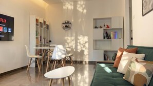 Ein modernes Wohnzimmer mit einem grünen Sofa, weißen Stühlen, einem Esstisch und Bücherregalen.