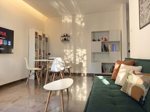 Ein modernes Wohnzimmer mit einem grünen Sofa, weißen Stühlen, einem Esstisch und Bücherregalen.