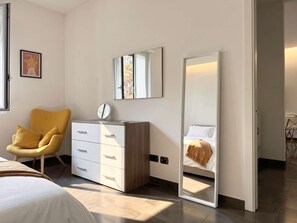 Ein Schlafzimmer mit einem Bett, einem Schminktisch, einem Stuhl, einem Spiegel und einer Tür.