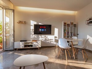 A modern living room with a flat-screen TV, a dining area with white chairs, a bookshelf, and a sliding glass door. - Casa Bonvicino, Città Studi (Milano)
