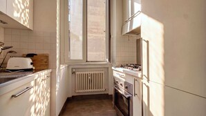 Eine schmale Küche mit Fenster, einer Toastmaschine, einem Herd und einem Kühlschrank.