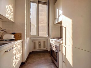 Eine schmale Küche mit Fenster, einer Toastmaschine, einem Herd und einem Kühlschrank.