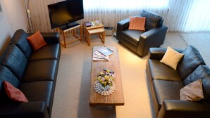Ein Wohnzimmer mit einer Couch, einem Couchtisch mit Blumen, einem Fernseher und einer Lampe.