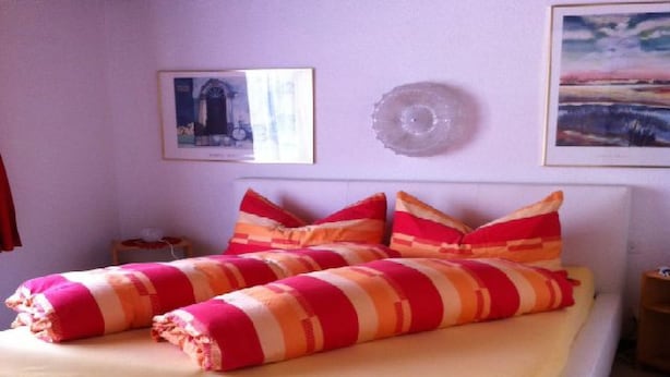 Ein Bett mit gestreifter Bettwäsche, ein Nachttisch und zwei gerahmte Bilder an der Wand.