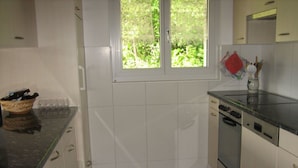 A kitchen with white cabinets, a dishwasher, and a window with a view of greenery.
