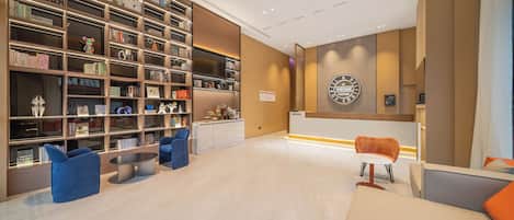 A modern hotel lobby with a large bookshelf, seating areas, and a reception desk.
