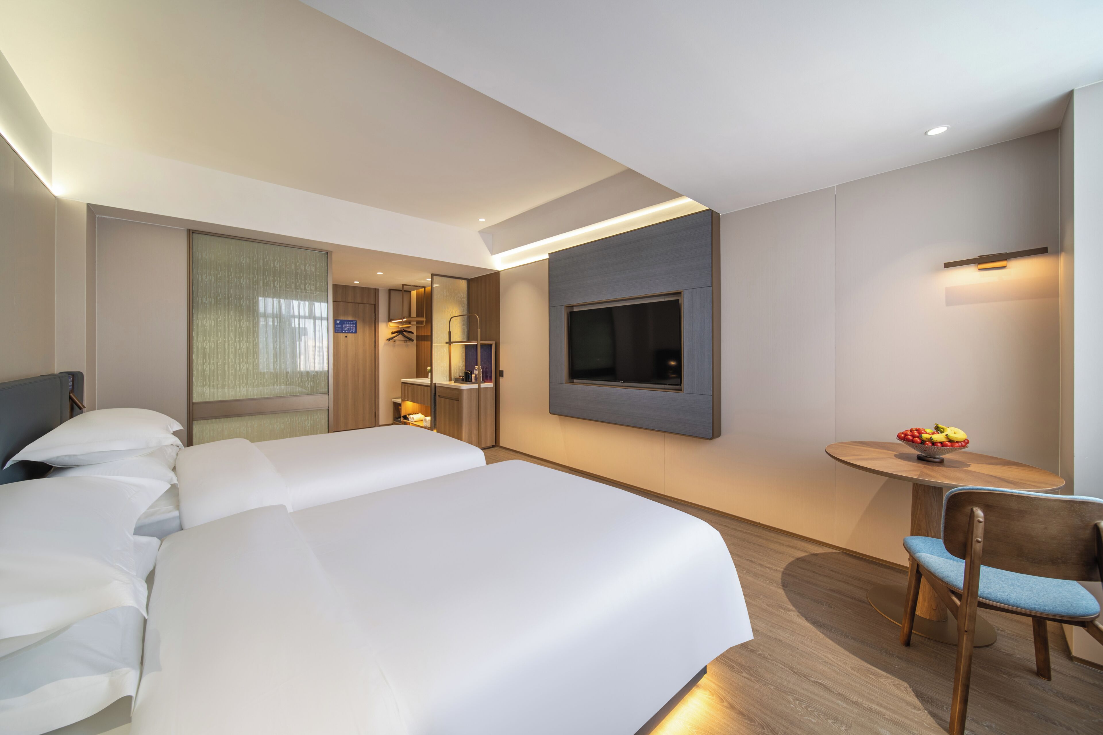 Habitación de hotel con una cama grande, un televisor montado en la pared, una mesita con un frutero y una zona de estar con un sillón.
