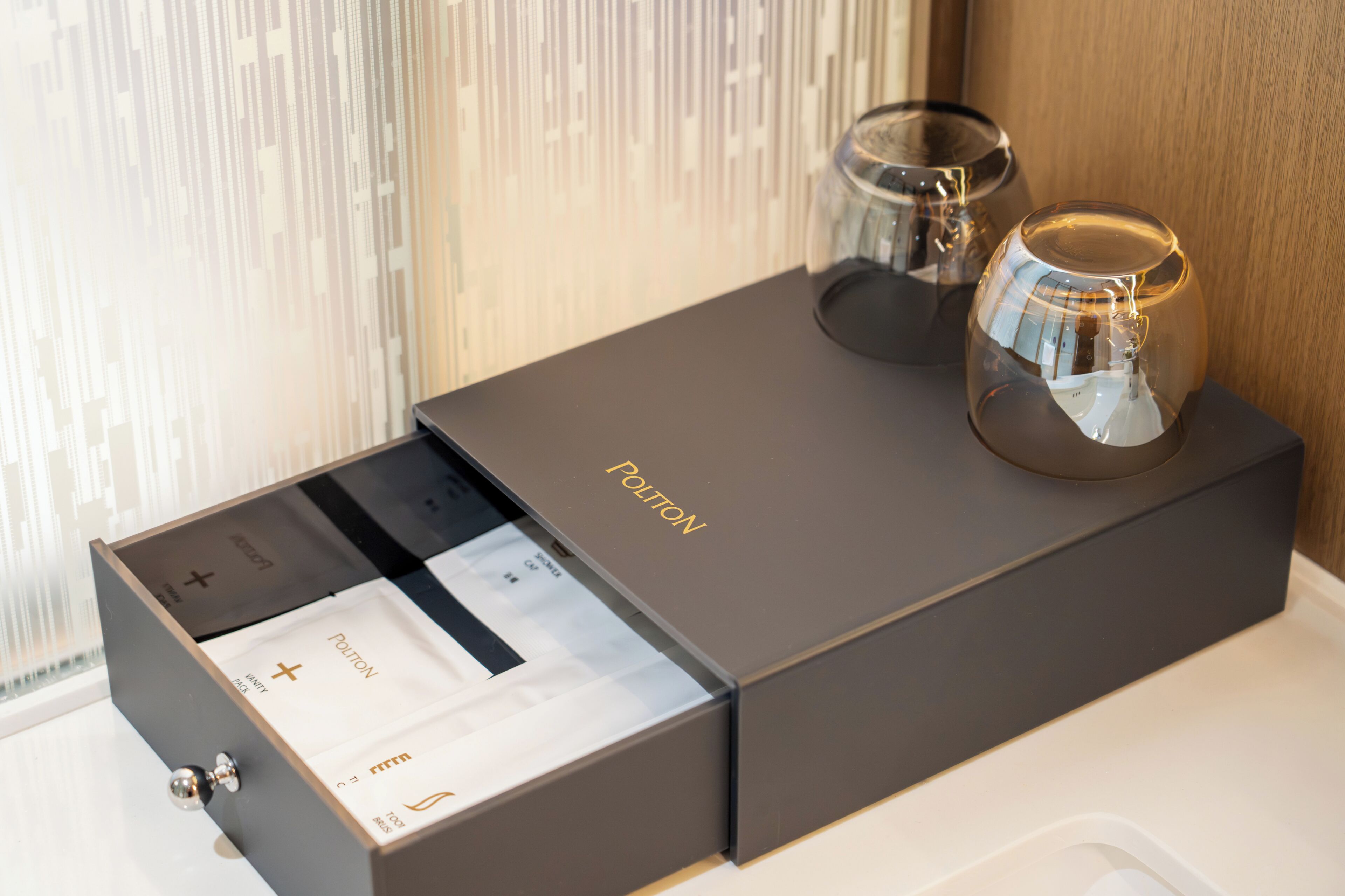 A dark-colored box with the word 'POLITON' on it, a drawer with a metallic knob, and two clear glass objects on top.