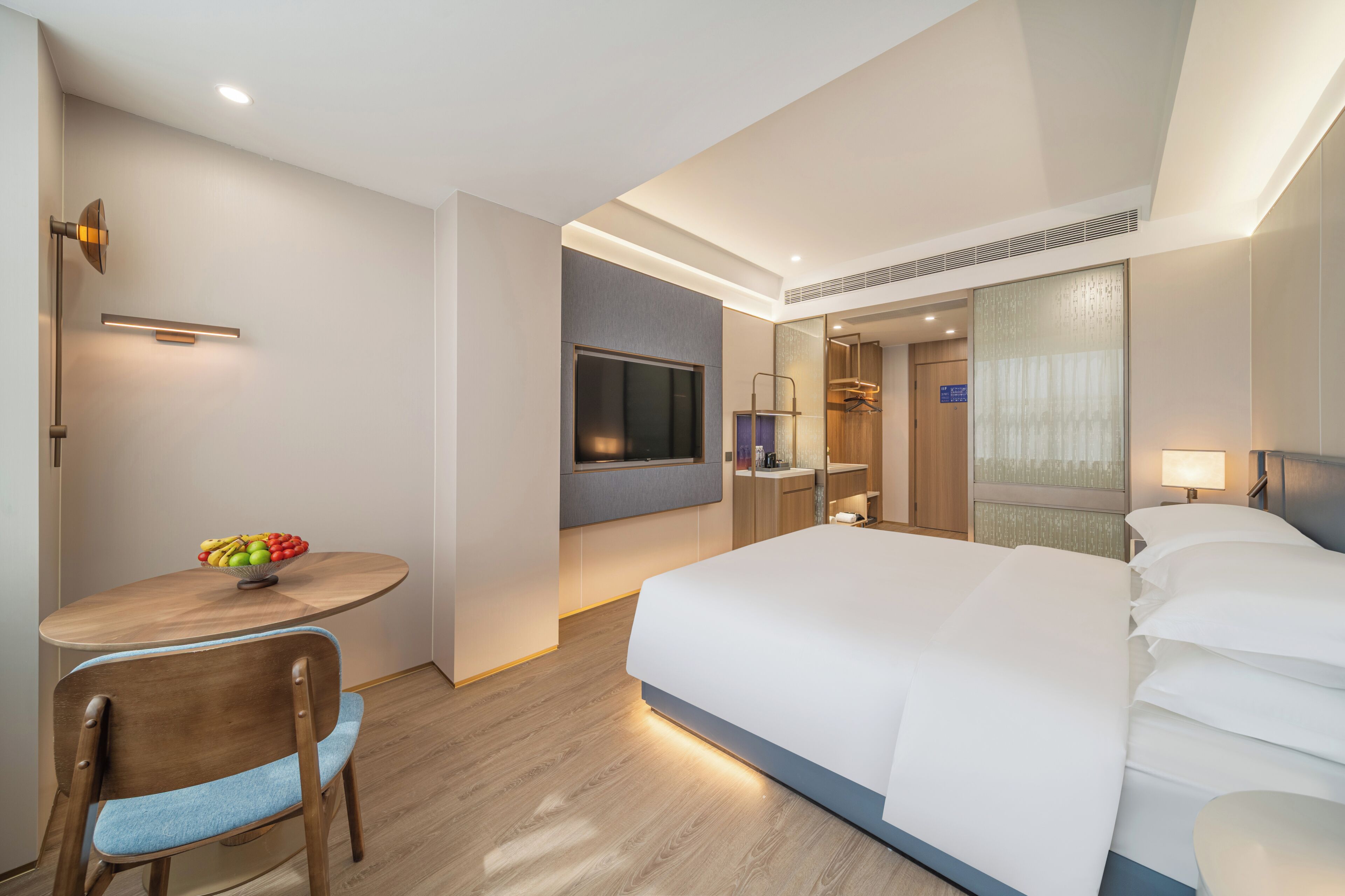 Habitación de hotel con cama, escritorio con frutero, silla, televisor y espejo.