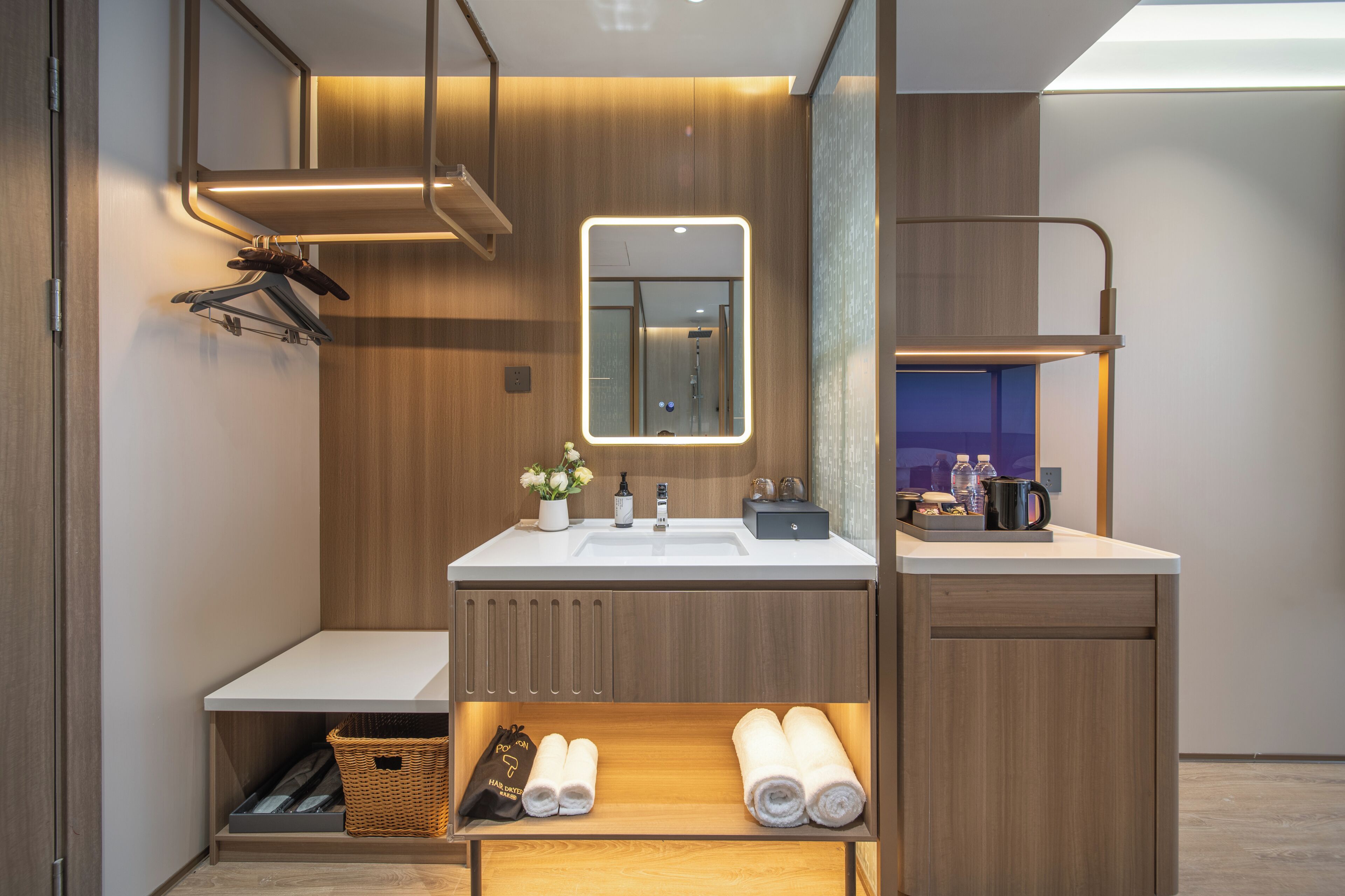 Un baño moderno con tocador de madera, un espejo y estante con toallas y artículos de aseo.