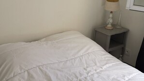 Uma cama com edredão branco, uma mesa de cabeceira com abajur e um espelho na parede.