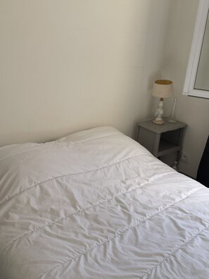 Ein Bett mit weißer Bettdecke, ein Nachttisch mit Lampe und ein Spiegel an der Wand.