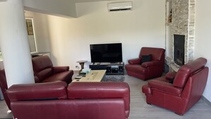 Uma sala de estar com sofás de couro vermelho, televisão de tela plana, lareira e parede de pedra.