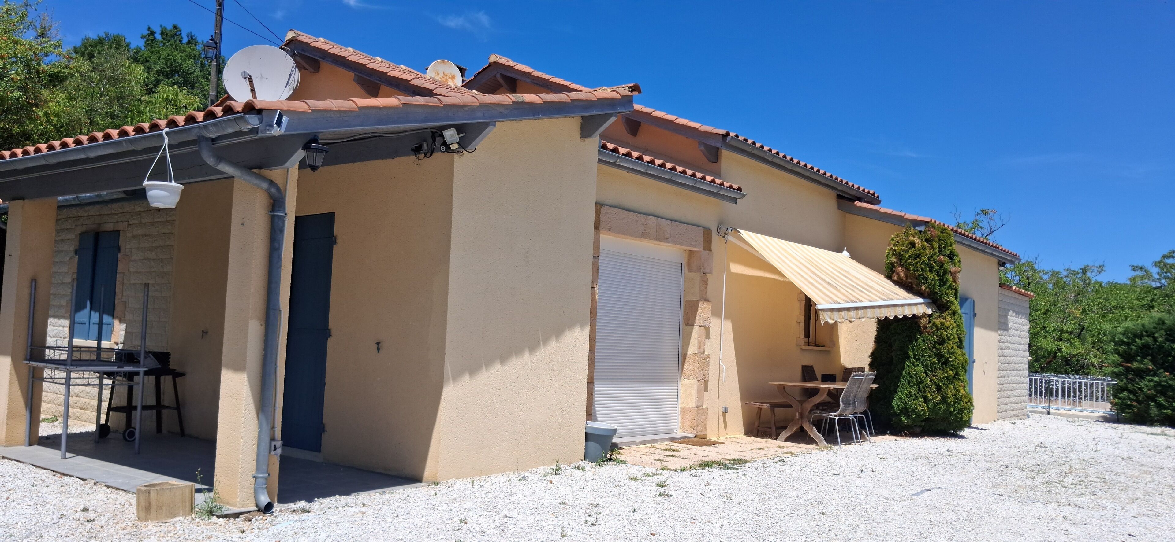 A single-story building with a tiled roof, a covered outdoor seating area, and a gravel driveway.