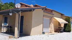 Um edifício térreo com telhado de cerâmica, área de estar coberta ao ar livre e entrada com caminho de cascalho.