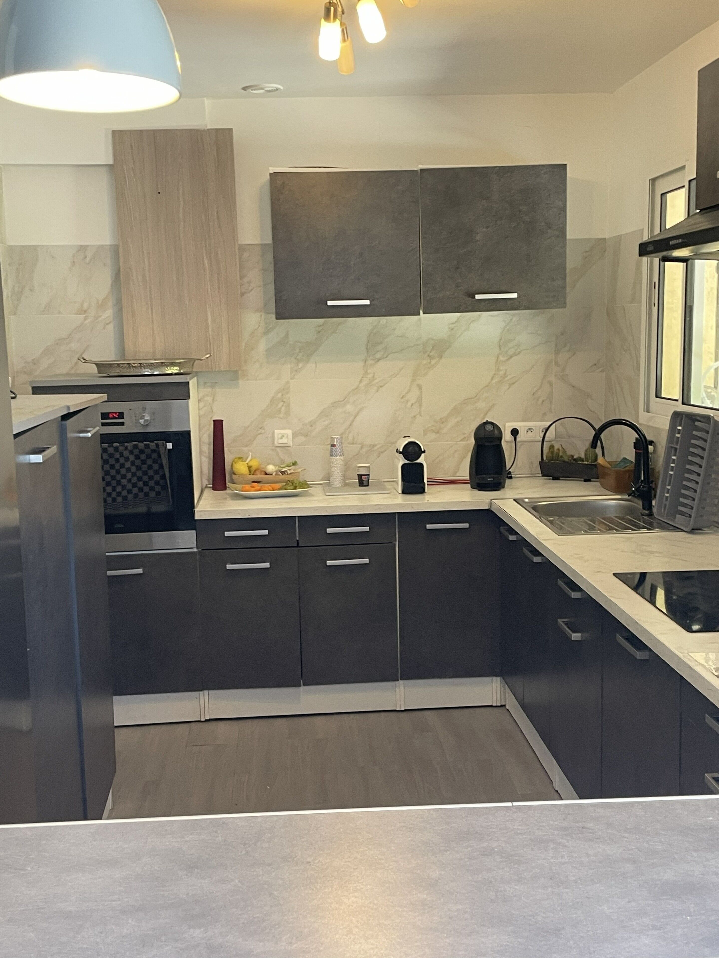 A modern kitchen with dark cabinetry, a marble countertop, and a built-in oven.