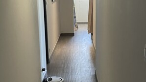 Um corredor estreito com um aspirador robô, uma porta no final e uma janela com cortinas.