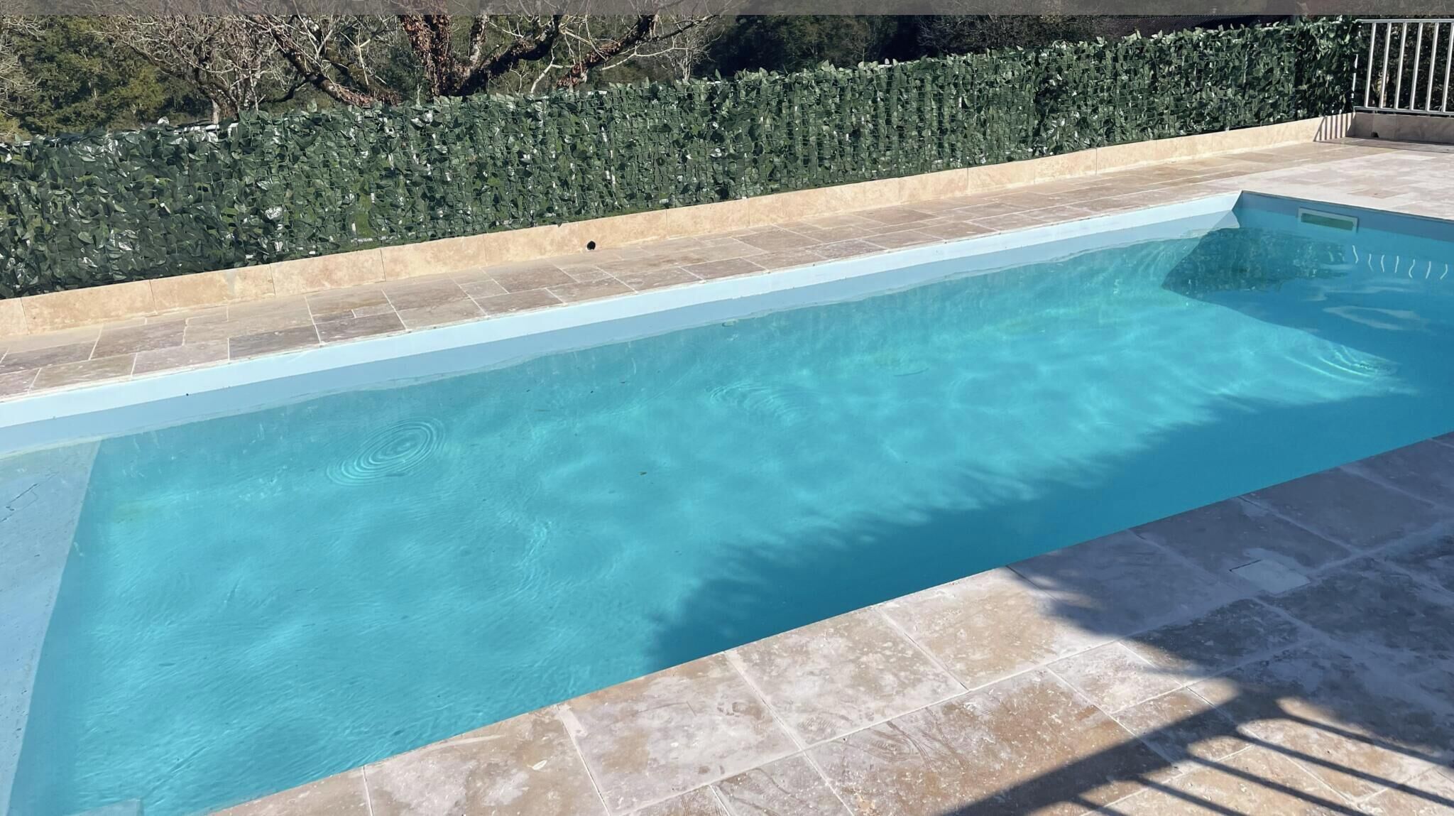 Una piscina rectangular con agua azul cristalina, rodeada por un deck de baldosas y un muro de piedra bajo.