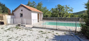 Ein kleines Gebäude mit einem Ziegeldach, einem umzäunten Swimmingpool und einem Kiesplatz.