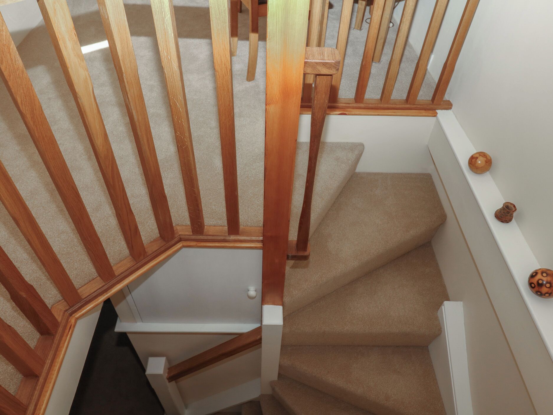 Una escalera de madera con peldaños cubiertos de alfombra color beige y paredes blancas.
