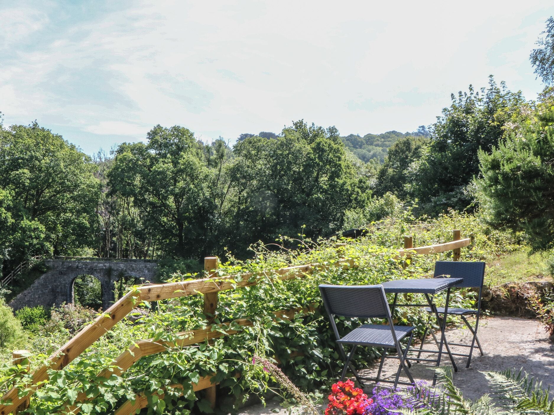 Un jardín con un puente de piedra, un enrejado de madera y mobiliario exterior.