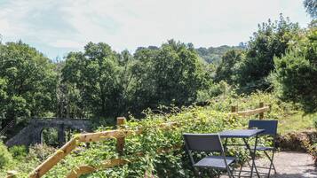 Un jardín con un puente de piedra, un enrejado de madera y mobiliario exterior.