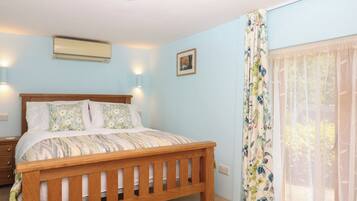Un dormitorio con cama de madera, una mesita de noche, aire acondicionado montado en la pared y una ventana con cortinas florales.